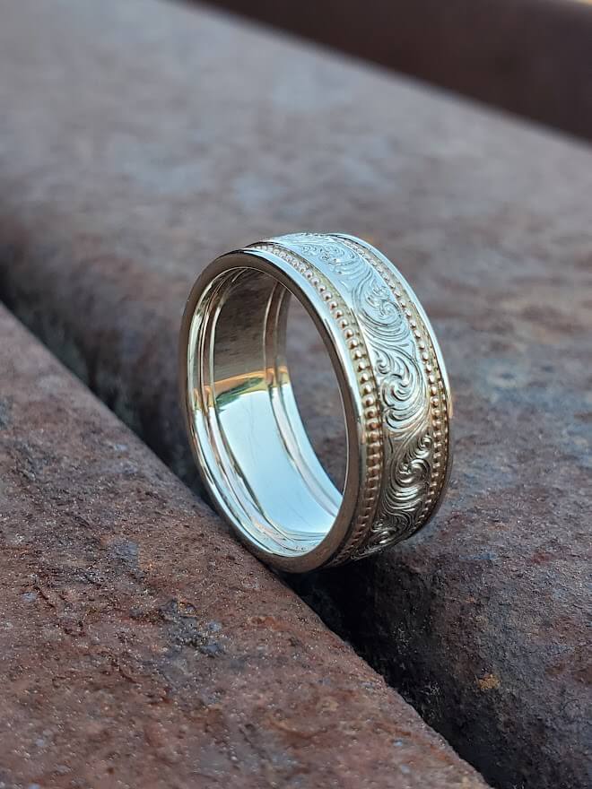 A hand-engraved men's western wedding band with rose and white gold sits on steel beams.