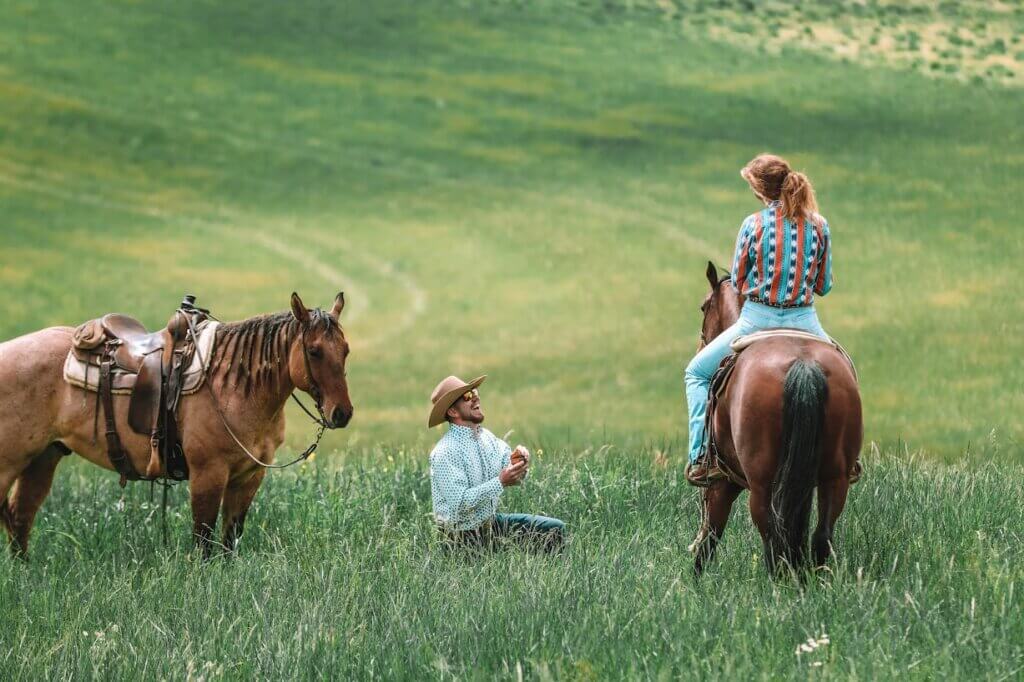 A quintessential western proposal takes place with a man on his knees in a field, asking a woman on a horse to marry him.