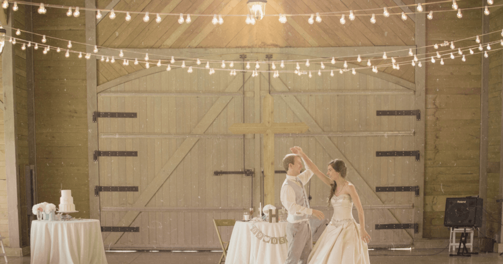 A newlywed couple dances in a barn strung with fairy lights.